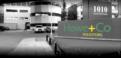 Outside of Howe + Co offices, in grey with the focus on the Howe + Co sign with address picked out in green and yellow lettering. 